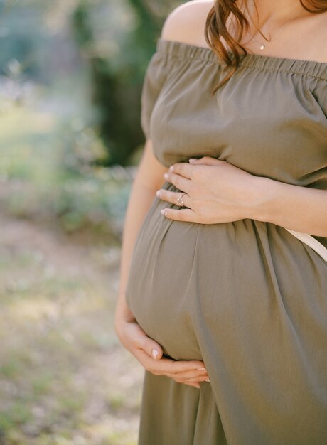 Kobieta w ciąży w zielonej sukience wspiera brzuch rękami