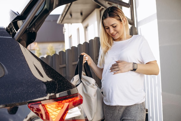 Kobieta w ciąży wkłada torbę z zakupami do bagażnika samochodu