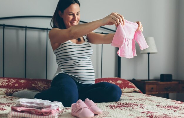 Kobieta w ciąży wyglądająca ubrania i buty dla dziewczynki Selektywna koncentracja na kardigan dla niemowląt