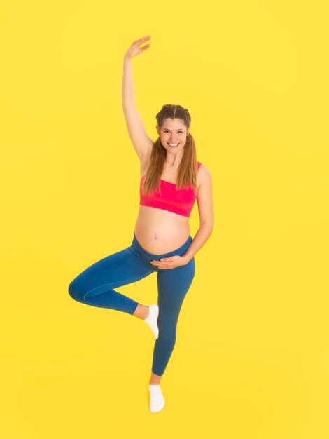Zdjęcie kobieta w ciąży wykonująca ćwiczenia jogi w pozie drzewa z podniesioną ręką w studio
