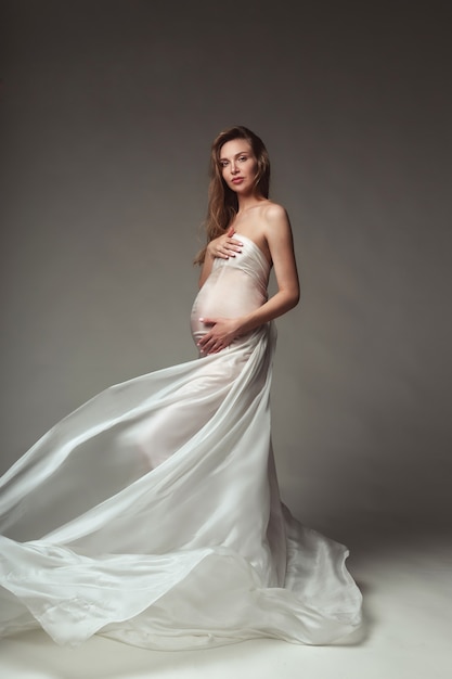Zdjęcie kobieta w ciąży z białym latającym jedwabiem na szarym tle