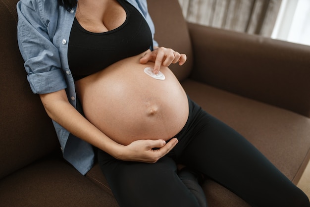 Kobieta w ciąży z brzuchem relaksuje na kanapie w domu. Ciąża, spokój w okresie prenatalnym. Przyszła mama odpoczywa w sypialni, zdrowy tryb życia