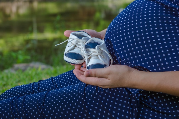 Kobieta w ciąży z butami przyszłego dziecka w dłoni i na brzuchu koncepcja macierzyństwa