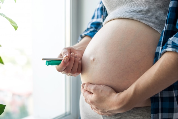 Kobieta w ciąży z dużym brzuchem trzyma papierosa i zapalniczkę