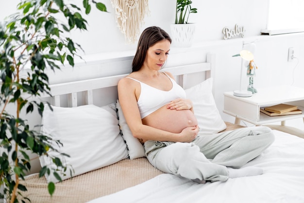 Kobieta w ciąży z dużym otwartym brzuchem na łóżku w domu marzy o urodzeniu dziecka Przyszła mama czeka i przygotowuje się do narodzin dziecka w jasnej sypialni