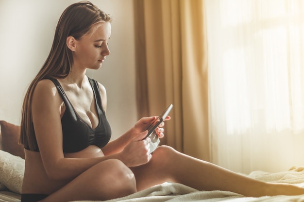 Kobieta W Ciąży Z Nowoczesnym Tabletem, Siedząc Na łóżku I Dopasowując Jej Długie Włosy