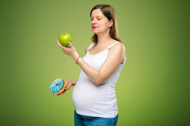 Kobieta w ciąży z pączkiem i zielonym jabłkiem radzi, jakie produkty powinnaś jeść