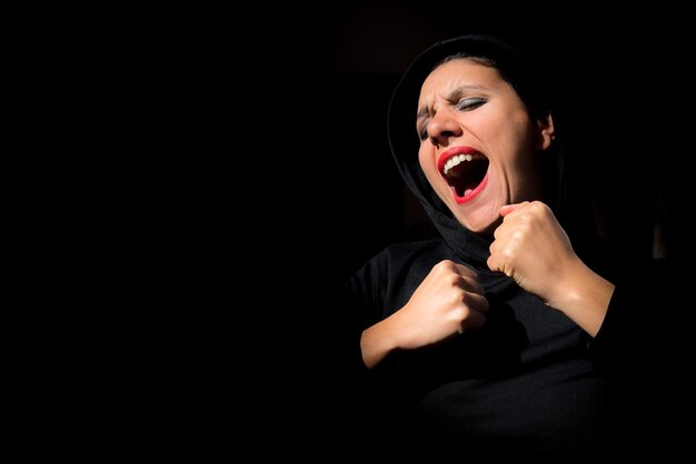 Kobieta w ciemności krzyczy z zaciśniętymi pięściami na czarnym tle