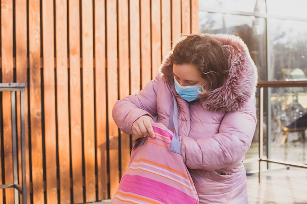 Kobieta w ciepłym płaszczu po zakupach trzymająca bawełnianą torbę z zakupami Słoneczny zimowy poranek przed supermarketem