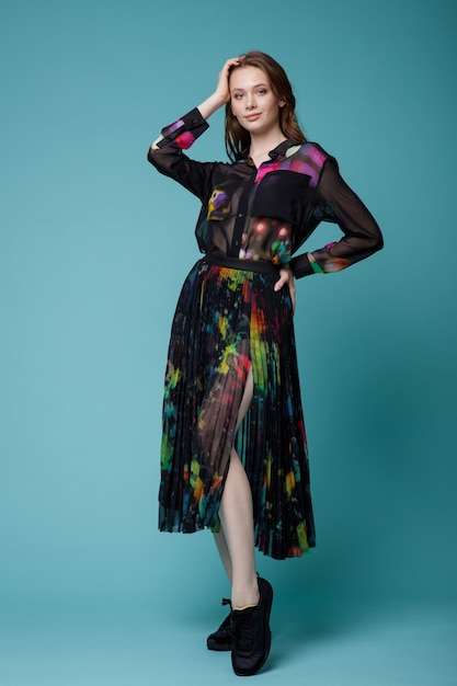 Kobieta w czarnej długiej spódnicy koszula kolorowe wzory trampki na turkusowym tle Studio Shot