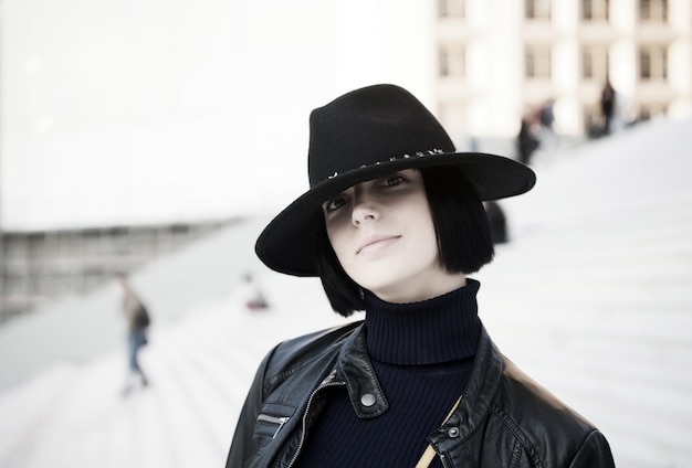 Kobieta w czarnym kapeluszu i kurtce pozuje na schodach Dziewczyna z naturalnym makijażem twarz i brunetki na zewnątrz Ambicja wyzwanie sukces koncepcja Moda i dodatki Styl urody Paryska kobieta