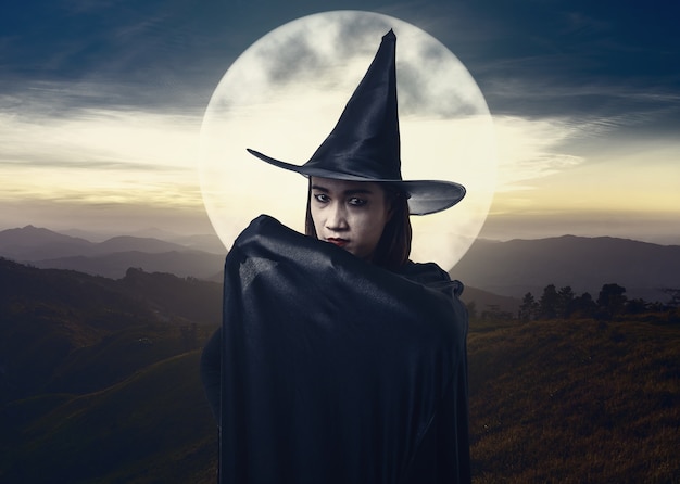 Zdjęcie kobieta w czarnym strasznym czarownicy halloween kostiumu z blaskiem księżyca. krajobraz góra i morze mgły