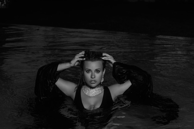 Kobieta w czarnym topie stoi w wodzie na ciemnym tle.