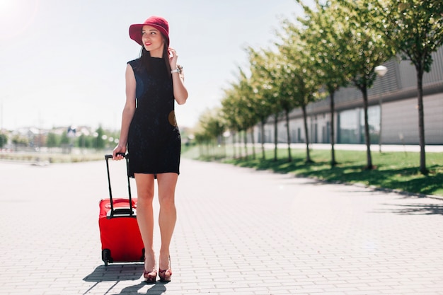 Kobieta w czerwonym kapeluszu idzie z czerwoną walizką na zewnątrz