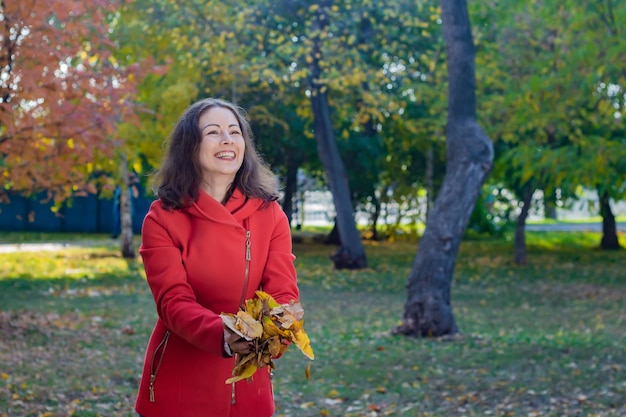 Kobieta w czerwonym płaszczu przygotowana do rzucania jesiennych liści w parku