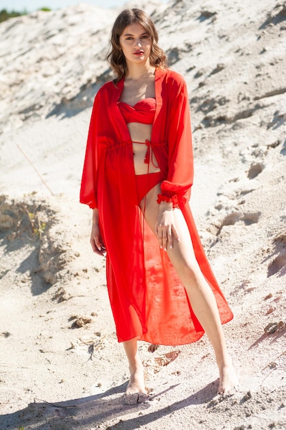 Kobieta w czerwonym stroju kąpielowym stoi na piaszczystej plaży.