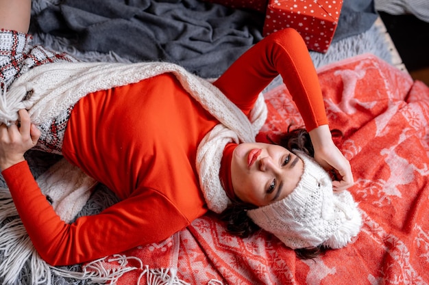 Kobieta w czerwonym swetrze i białym kapeluszu na łóżku, pozowanie do kamery. Szczęśliwego Nowego Roku i wesołych świąt zdjęcie koncepcji