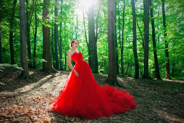 Kobieta w długiej czerwonej sukience i królewskiej koronie w mglistym lesie