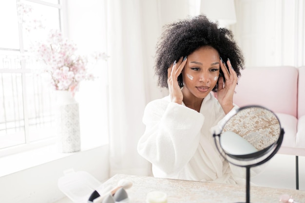 Kobieta w domu używa nowego kremu do twarzy Kobieta zajmuje się pielęgnacją skóry przy pomocy kosmetyków