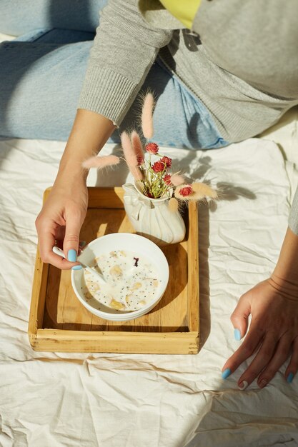 Kobieta W Dżinsach Siedzi Na łóżku I Je Zdrową Miskę Muesli Podczas Porannego Słońca, śniadanie W łóżku.