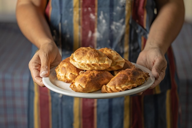 Kobieta w fartuchu poplamionym mąką, trzymająca tacę z argentyńskimi empanadas