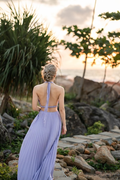 Kobieta w fioletowej sukience chodzić po kamiennym chodniku na plaży, cieszyć się romantycznym momentem zachodu słońca.