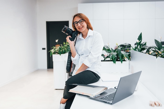Kobieta w formalnych ubraniach i z kamerą siedząca w biurze