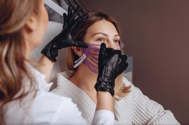 Kobieta w gabinecie kosmetycznym zostaje poddana zabiegowi tapingu, aby napiąć skórę jej twarzy