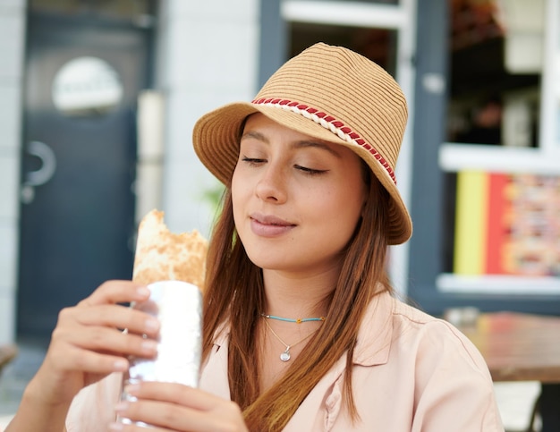 Kobieta w kapeluszu jedząca kebaba w ulicznej kawiarni