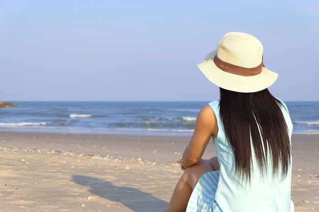 Kobieta w kapeluszu siedząca na plaży na tle nieba