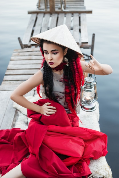 Kobieta w kapeluszu w stylu azjatyckim siedzi na drewnianym moście