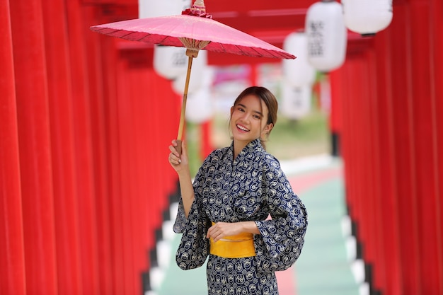 kobieta w kimono, trzymając parasol, wchodząc do świątyni w ogrodzie japońskim.