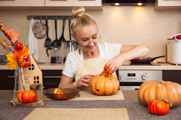 Kobieta w kuchni wyciąga pestki dyni na Halloween w pokoju o jesiennym wystroju i latarni. Przytulny dom i przygotowanie do Halloween