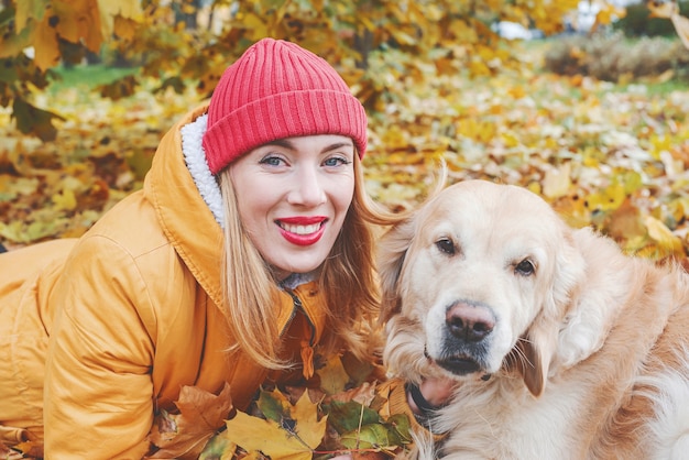 Kobieta w kurtce i pies retriever wśród żółtych jesiennych liści w parku.