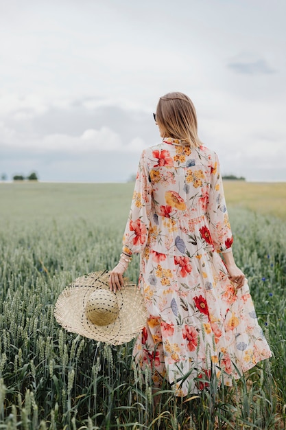 Kobieta w kwiecistej sukience z tkanym kapeluszem na polu