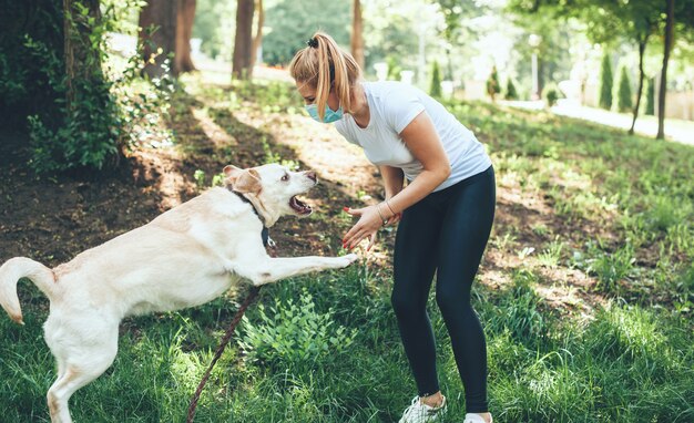 kobieta w masce bawi się w parku ze swoim golden retriever