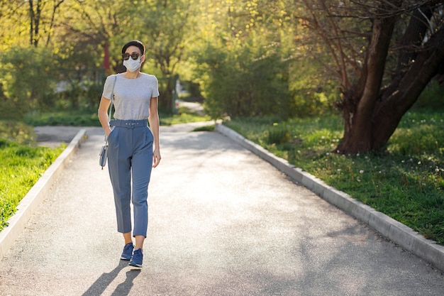 Kobieta w masce medycznej samotnie spaceruje po parku podczas epidemii Covid 19. Ochrona w profilaktyce koronawirusa. Koncepcja dystansu społecznego.