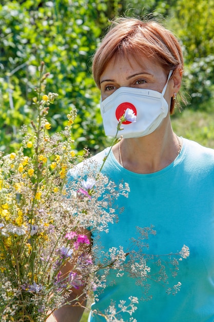 Kobieta w masce ochronnej trzymająca bukiet polnych kwiatów i próbująca walczyć z alergią na pyłki.