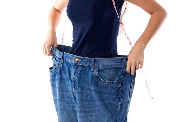 Kobieta w niebieskiej koszulce z centymetrem wokół szyi trzymająca dżinsy znacznie większego rozmiaru