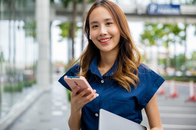 Kobieta w niebieskiej koszuli wygląda na zadowoloną, przeglądając swój smartfon na miejskiej ulicy