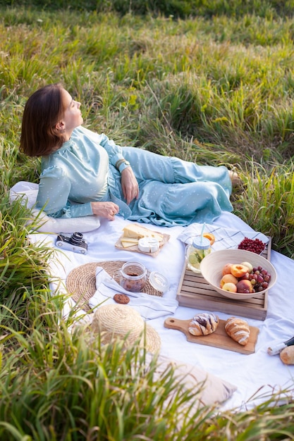 Kobieta w niebieskiej sukience siedzi na pikniku w parku z panoramicznym widokiem