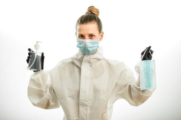 Kobieta w odzież ochronną trzyma maskę i dezynfektor w jej ręce.