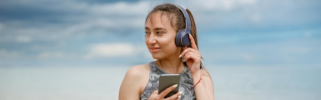 Kobieta w odzieży sportowej słuchająca muzyki na słuchawkach przy plaży na tle oceanu