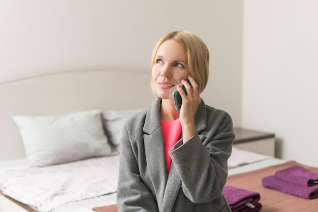 Kobieta w odzieży wierzchniej siedząca na łóżku z telefonem