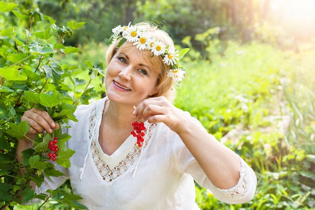 Kobieta w ogrodzie, zbierz czerwone jagody. Uśmiecha się kobieta w średnim wieku. Pokazuje owoce.