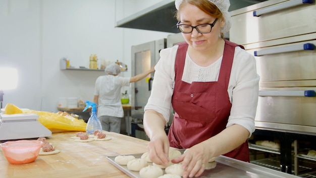 Kobieta w okularach i fartuchu piecze ciasta w piekarni, zbliżenie