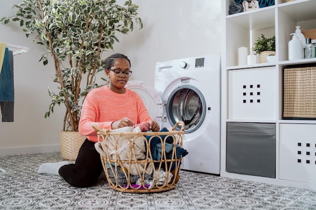 Kobieta w okularach wykonuje prace domowe w łazience, pralnia klęczy z wiklinowym koszem
