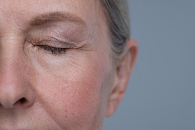 Kobieta w podeszłym wieku ze starzejącą się skórą na szarym tle zbliżenie i przestrzeń dla tekstu Leczenie odmłodzenia