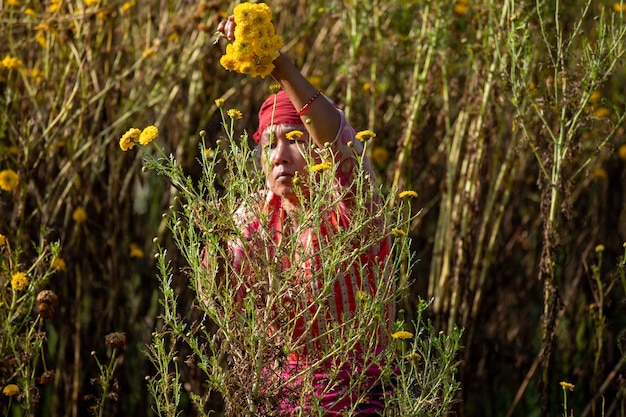 Kobieta w polu kwiatów trzyma żółty kwiat.