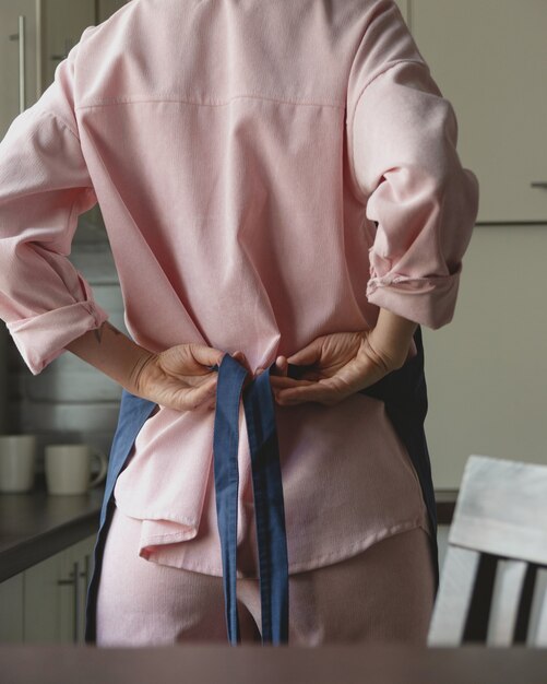 Kobieta W Różowym Garniturze Zawiązuje Na Plecach Niebieski Fartuch, Aby Zacząć Gotować W Swojej Domowej Kuchni Bez Twarzy